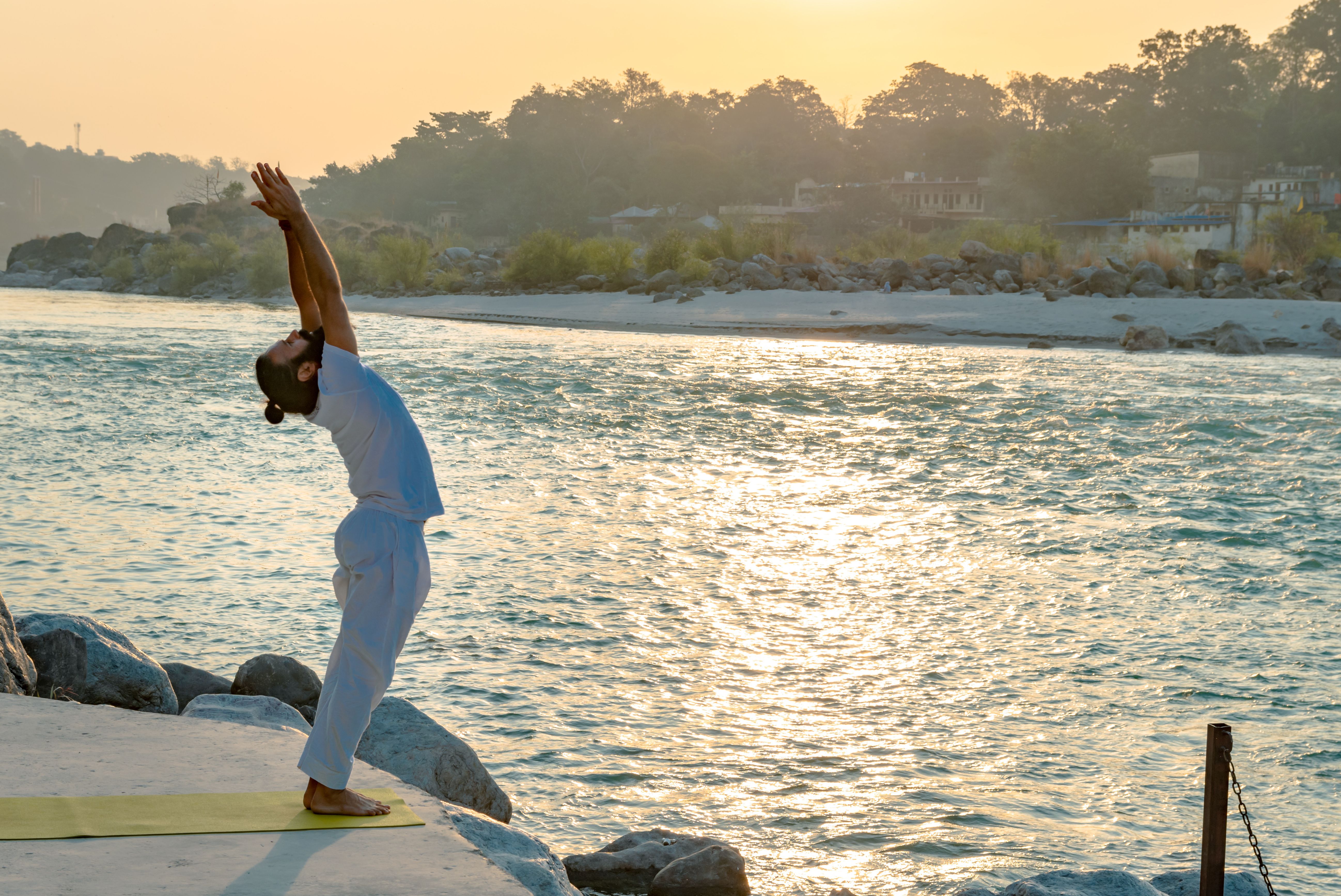 A yogi seated in deep meditation on the banks of the River Ganga at sunrise in Rishikesh, with the Himalayan mountains rising in the morning mist behind