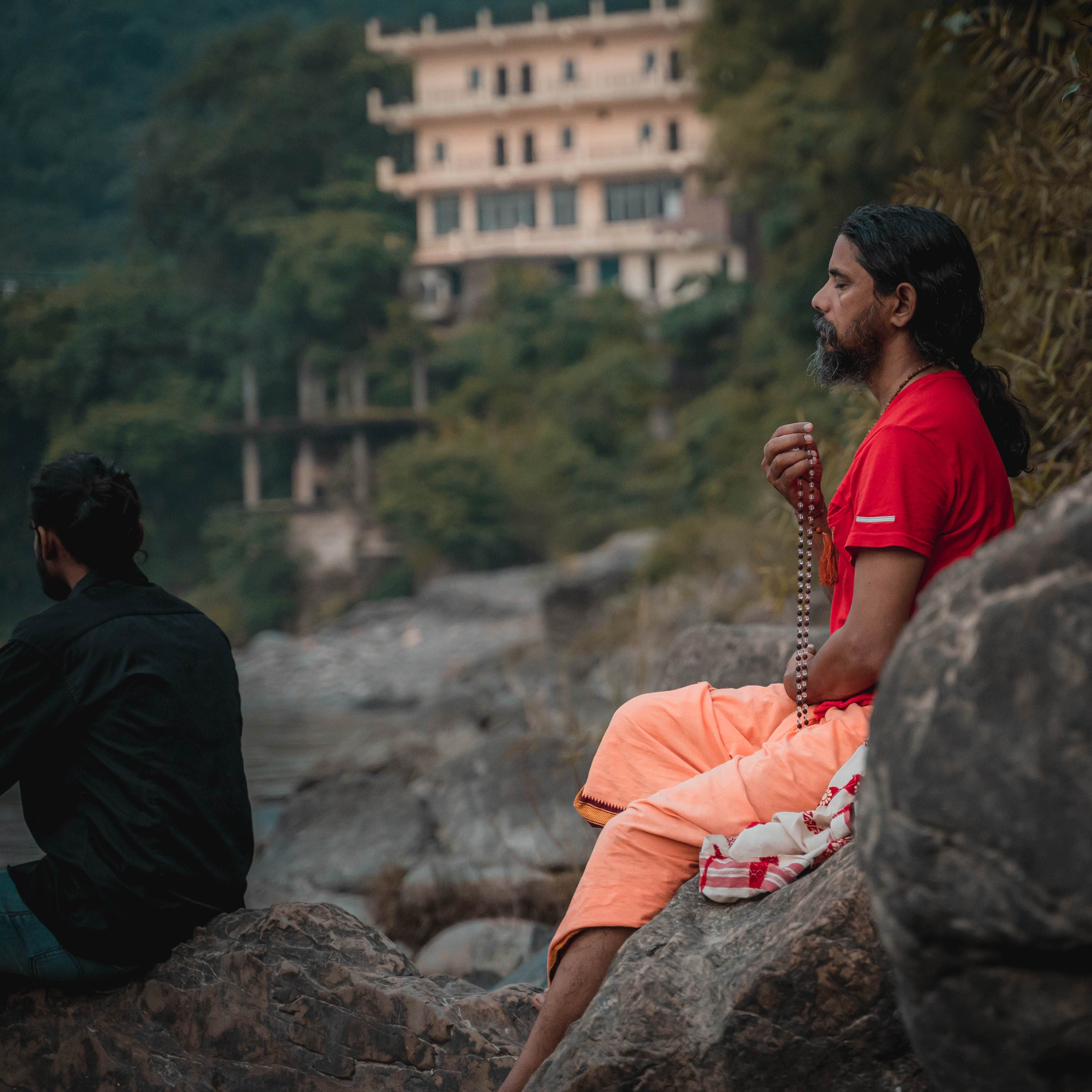 A yogi demonstrating the Trikonasana triangle pose on a wooden platform with the Ganga river visible in the background